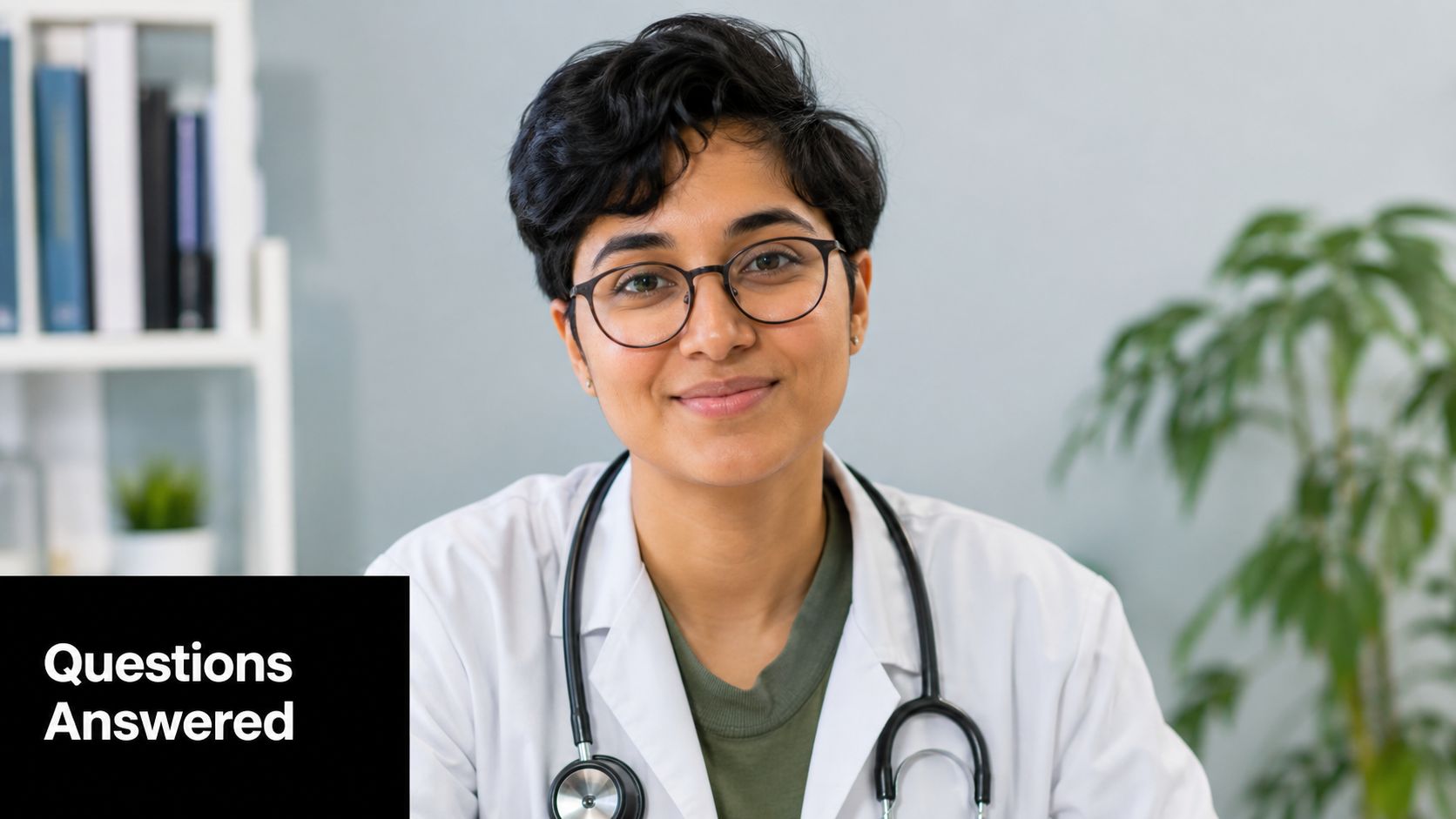 A friendly young female doctor with short hair and a stethoscope sitting in her medical office.